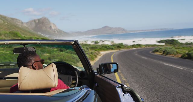 African american man wearing sunglasses stepping out of convertible car on road. road trip travel and adventure concept
