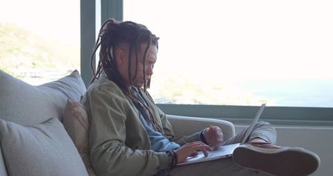 African american man working on laptop in coastal lounge, relaxed remote work lifestyle