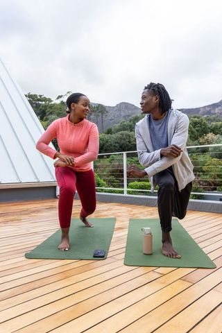 African american couple practicing balance lunges on rooftop yoga mats with mountain view