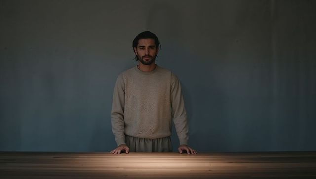 Man standing behind wooden table resting hands under spotlight on gray backdrop