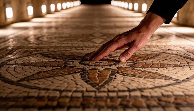 Hand touching ancient mosaic floor in lit corridor — close-up texture and pattern