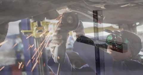 Female mechanic grinding under car with angle grinder sparks flying in auto workshop bay
