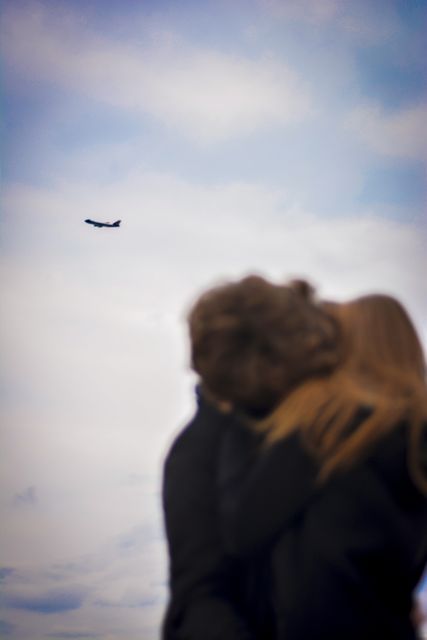 Scene depicts couple hugging outdoors while watching airplane in the sky. Ideal for themes emphasizing romance, love, travel, or shared adventures. Suitable for use in travel blogs, advertisements for romantic vacations, or conceptual displays of relationship and togetherness.