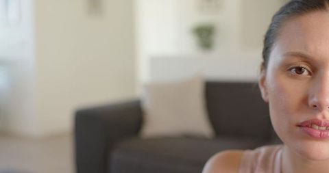 Pensive woman gazing left in minimalist living room closeup with neutral sofa and plant