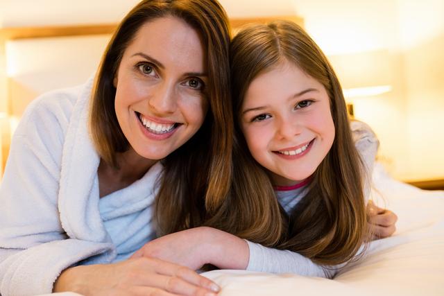 This image shows a joyful mother and daughter lying on a bed in a cozy bedroom. Both are smiling warmly, showcasing a strong bond and affection. Ideal for use in family-oriented advertisements, parenting blogs, home decor promotions, and articles about family relationships and bonding.