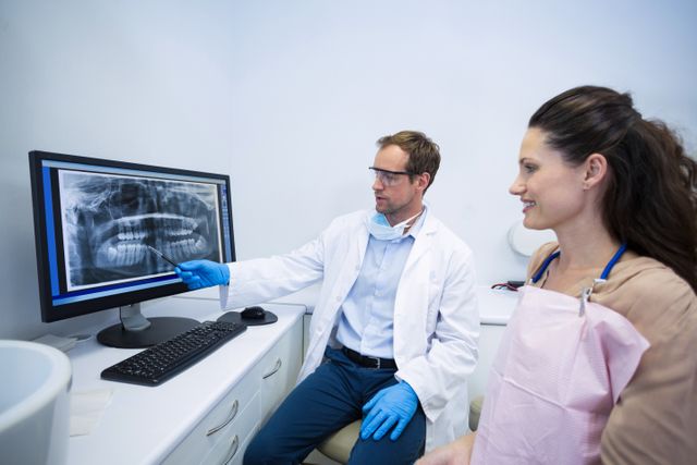 Dentist wearing white coat and gloves explaining dental x-ray to female patient in dental clinic. Ideal for use in healthcare, dental care, and medical consultation contexts. Suitable for illustrating dental examinations, patient education, and professional dental services.