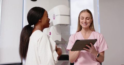Mammography tech guiding African American woman through breast screening holding tablet