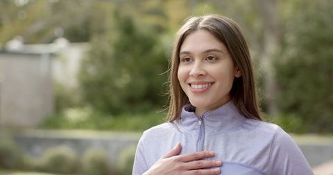 Young woman expressing gratitude outdoors with hand on chest, serene smile in lavender top