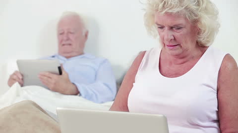 Elderly Couple Using Technology Together in Bed