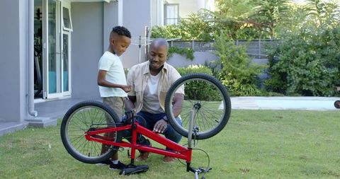 Father teaching son to fix bicycle outdoors in sunny backyard