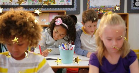Elementary students writing and concentrating at desks with decorative gold stars