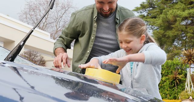 Father and daughter are laughing and focusing on cleaning the car's windshield. The scene demonstrates outdoor family bonding through engaging in household tasks. Ideal for illustrating concepts related to parenting, family, teamwork, outdoor activities, and responsible upbringing. It can be used in articles, blogs, advertisements, or social media posts focusing on parenting, family activities, or car care.