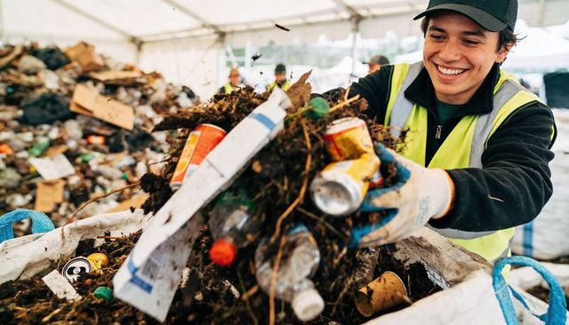Smiling recycling worker sorting organics, bottles and cans at outdoor sorting tent