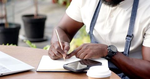 African american man writing in notebook at outdoor cafe patio