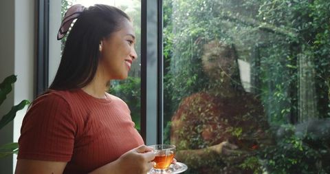 Mid Adult Woman Enjoying Tea Relaxing by Sunlit Window with Natural View