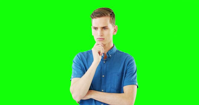 Young man in blue shirt contemplating with hand on chin against a bright green background. Perfect for illustrating critical thinking, decision making, or problem solving in educational content, blog posts, mental health discussions, and advertisements aimed at young adults.