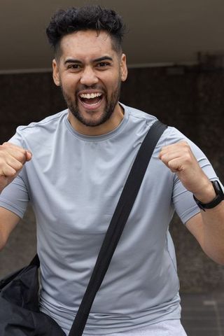 Young man celebrating victory raising fists wearing light gray gymwear with duffel strap