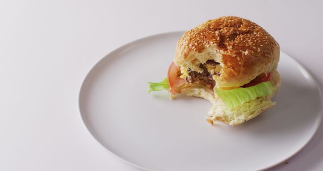 Shows a partially eaten burger on a white plate, featuring fresh lettuce, tomato, and a sesame bun. Ideal for food blogs, restaurant menus, and culinary ads promoting fast food or tasty burgers.