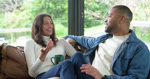 Couple relaxing on leather sofa sharing coffee, laughter and conversation by bright window