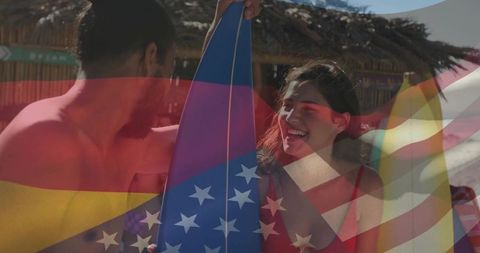 Smiling couple holding blue star surfboard on beach with patriotic flag overlay
