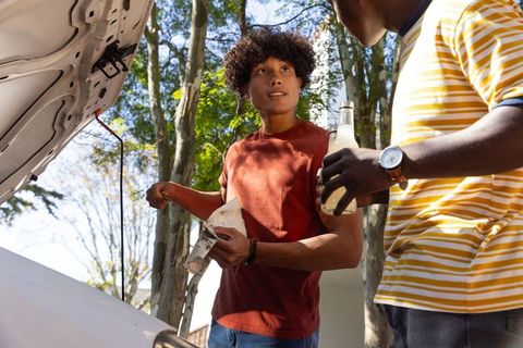 Young diverse friends checking car engine sharing drink during diy roadside maintenance