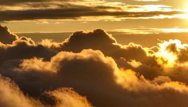 Golden sunset clouds drifting across sky with sunlit rims and dramatic light