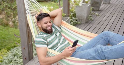hispanic man relaxing in hammock with smartphone on deck - Download Free Stock Images Pikwizard.com