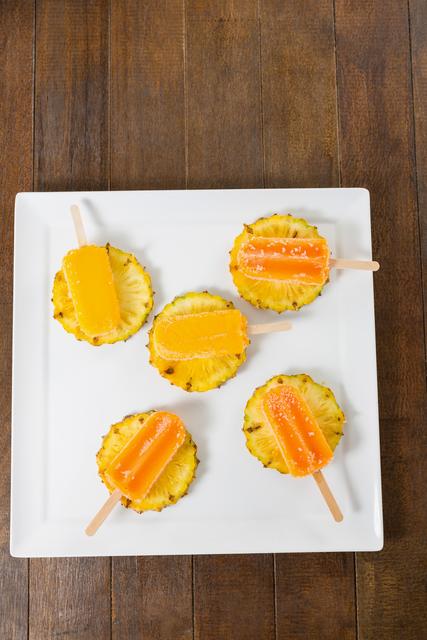 Refreshing pineapple ice lollies placed on pineapple slices on a square white plate. Ideal for summer-themed promotions, tropical dessert recipes, healthy snack ideas, and gourmet food presentations. Perfect for use in food blogs, social media posts, and culinary magazines.