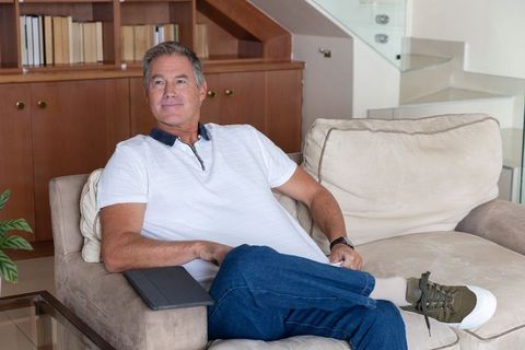Mature man relaxing on beige sofa with tablet, white polo and jeans, modern home leisure