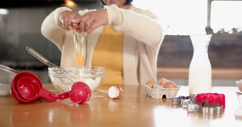 Elderly Woman Cracking Egg Baking Ingredients in Kitchen