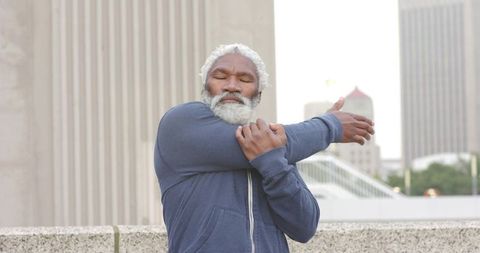 Senior African American Man Stretching Arm on City Rooftop Terrace in Navy Hoodie