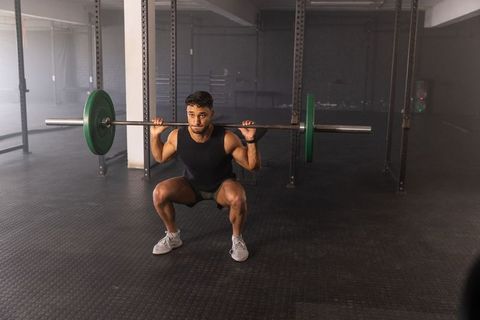 Determined athlete performing barbell back squat with green weight plates