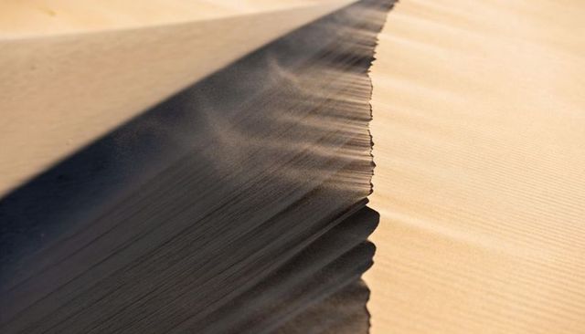 Wind-cut sand dune crest casting sharp diagonal shadow, minimalist desert ridge texture