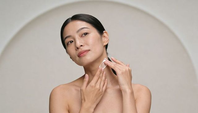 Asian woman applying neck cream with spatula for skincare routine minimalist portrait