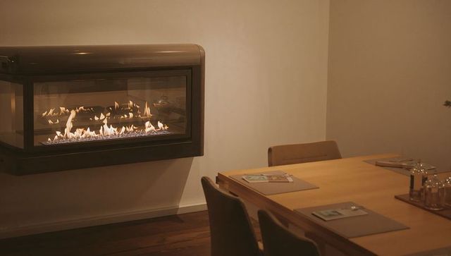 Minimalist dining room with wall-mounted glass fireplace emitting warm glow over wood table