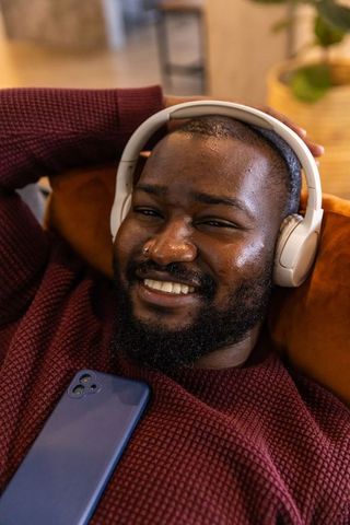 Relaxing african american man listening to music with white headphones, smiling