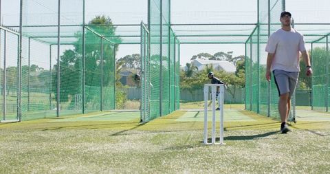 Cricket practice nets with batsman batting and coach walking on turf wicket training