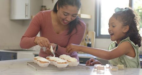 Mother and Daughter Decorating Cupcakes at Kitchen Counter Smiling Bonding Home Baking