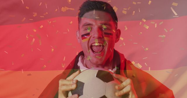 A highly enthusiastic soccer fan is celebrating his team's victory. He is shown with the German flag painted on his face while holding a soccer ball, and surrounded by colorful confetti. This image is ideal for use in articles related to sports events, advertisements for soccer events or tournaments, sports team promotions, and content emphasizing fan spirit and national pride.