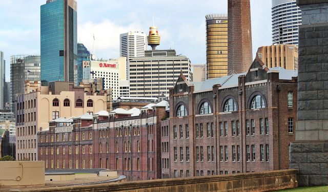 Historic brick buildings stand in contrast to Sydney's modern skyscrapers. The juxtaposition highlights the blend of old and new architectural styles. Useful for promoting urban tourism, historic preservation, and illustrating city growth.