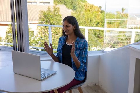 Woman video conferencing on laptop outdoors with ocean view