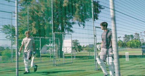 Two male cricketers training in batting nets with pads and gloves outdoor practice
