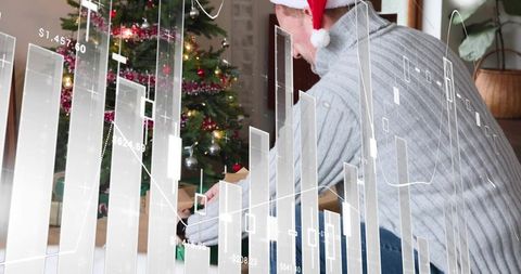Man wearing santa hat wrapping gifts by christmas tree with financial data overlay