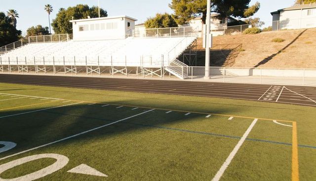 Empty athletic stadium with artificial turf, yard lines, bleachers, running track, press box