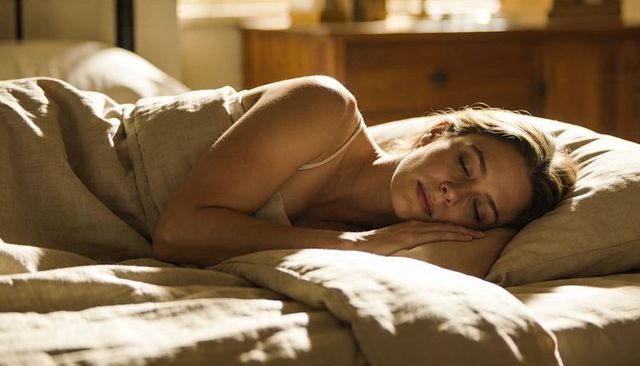Sunlit woman sleeping on linen bedding in cozy neutral bedroom, peaceful morning rest