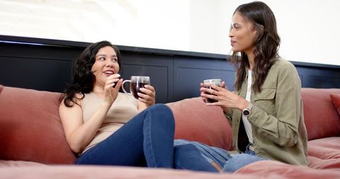 Friends chatting and sipping coffee on pink velvet sectional couch in modern living room