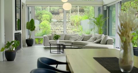 Sunlit minimalist living room with light-gray sectional, indoor plants and glass walls