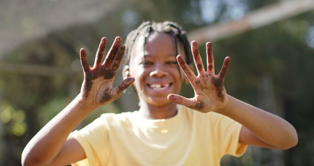 Happy african american boy standing, showing dirty hands and smiling in sunny vegetable garden. Nature, gardening, healthy life style, unaltered.