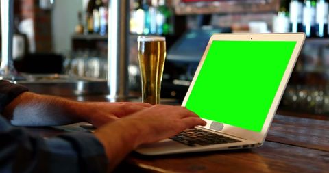 Person Using Laptop with Green Screen at Cozy Pub Counter