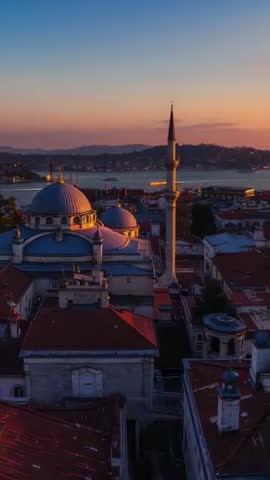 Vertical drone pull-back capturing mosque domes and minaret over coastal rooftops at sunset